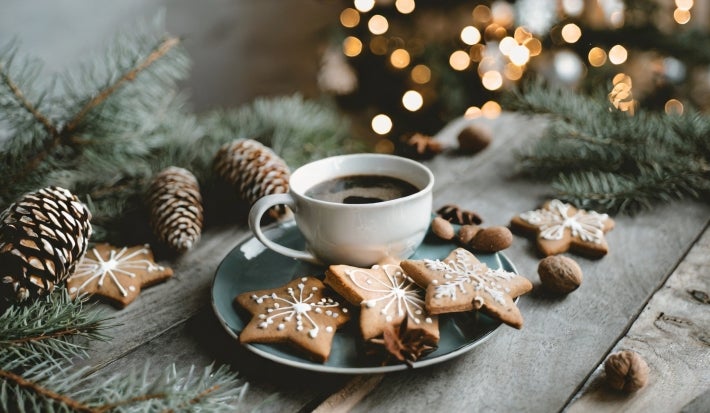 Em cima de uma mesa decorada pinhas e árvore de Natal, prato com três biscoitos em forma de estrela, decorados com açúcar de confeiteiro.