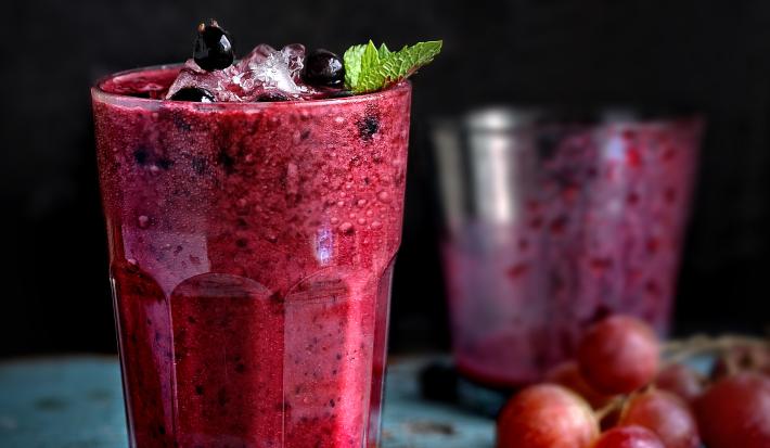 Fotografia em tom escuro de dois copos de vidro, o da frente está cheio com uma bebida de suco de uva com leite e neston, e o do fundo está quase vazio.