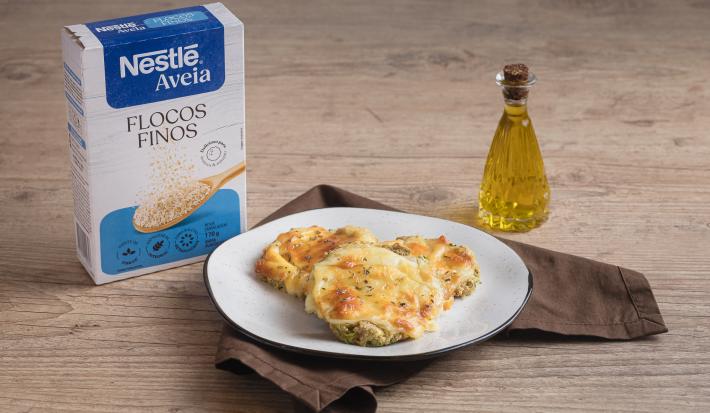Foto da receita de pizza de abobrinha com aveia servida em 3 porções em um prato branco sobre um pano marrom escuro em cima de uma mesa de madeira com um dispenser de azeite feito de vidro ao lado direito