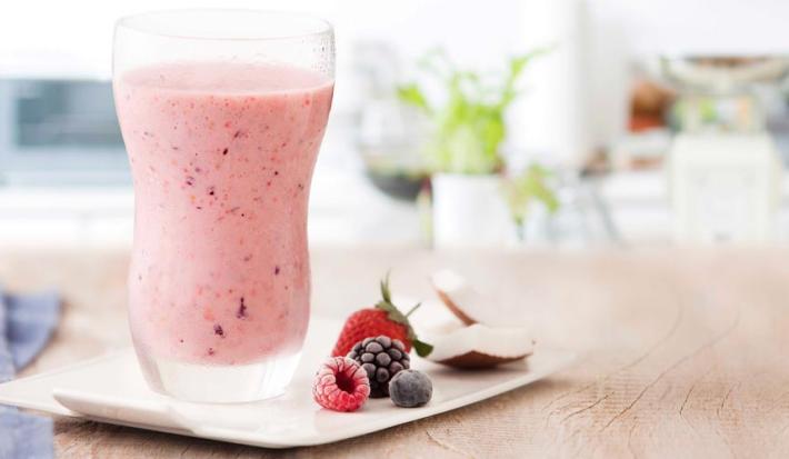 fotografia e tons de rosa e branco de uma bancada bege vista de frente, contém um copo transparente com a bebida de frutas vermelhas e ao lado contém frutas vermelhas.