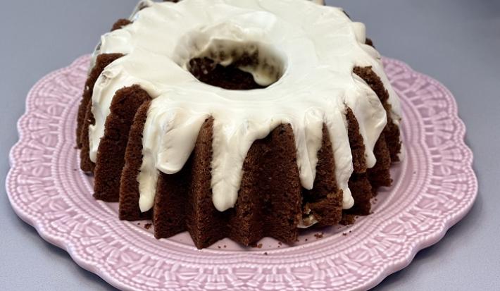 Foto da receita de bolo de cenoura carrot cake servida em uma porção inteira sobre um prato de porcelana cor de rosa em cima de uma mesa cinza