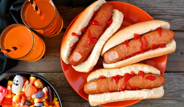 Cachorro-quente com salsichas em formato de dedo, pão macio e dourado, corte superficial na ponta simulando unha, com ketchup vermelho escorrendo.