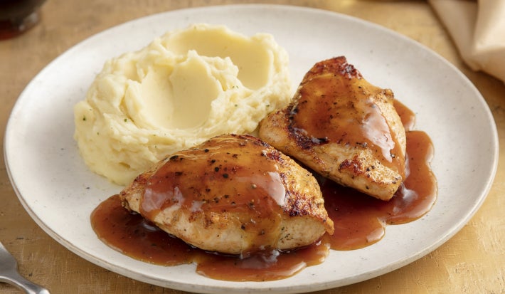 Pedaços de frango dourados servidos com purê cremoso de batata e molho escuro reduzido, apresentados em prato branco elegante