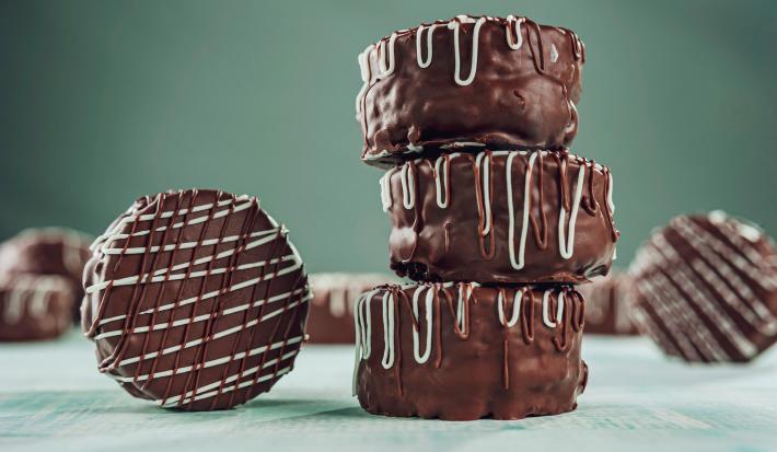 Imagem de três pães de mel empilhados e um ao lado. O pão de mel está decorado com riscos de chocolate branco e ao leite.