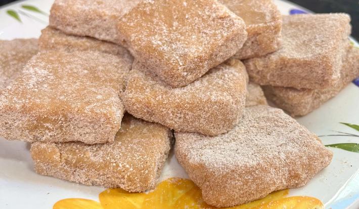Fotografia de vários quadradinhos de palha italiana de churros, passados no açúcar e canela. As unidades estão juntas e sobrepostas, apoiadas em um prato branco com desenhos coloridos