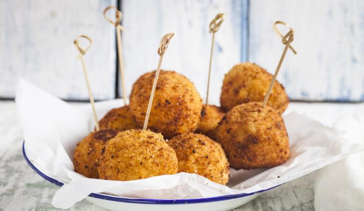 fotografia em tons de branco e bege de uma bancada cinza vista de frente. Contém um prato redondo branco com bolinhos de arroz frito, e por cima palitos.