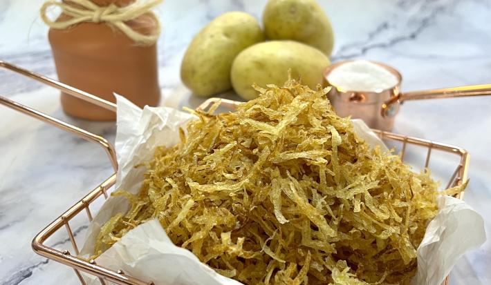Foto da receita de batata palha caseira. Observa-se a batata palha em uma cestinha de servir rose gold em cima de um mármore branco.