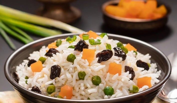Tigela marrom com arroz colorido com passas, ervilhas e cenouras picadas.
