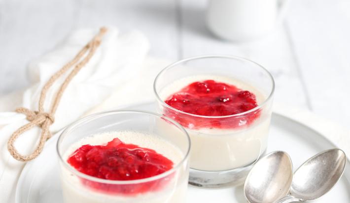 fotografia em tons de branco e vermelho tirada de um recipiente redondo branco, contém duas taças com mousse e calda de frutas vermelhas por cima