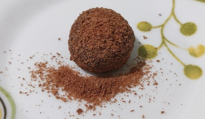 Foto da receita de Brigadeiro de Café. Observa-se um brigadeiro em um prato branco decorado com o café polvilhado por cima.