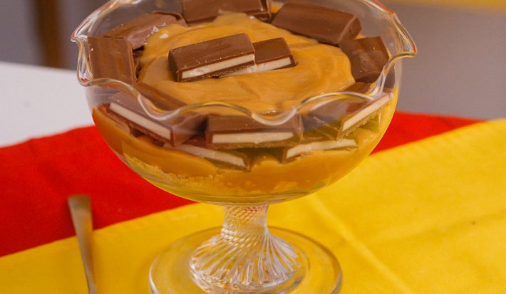 Taça de pavê com creme caramelizado e pedaços de chocolate, sobre toalha amarela e vermelha.