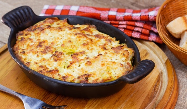 Em cima de uma mesa, refratário preto com queijo gratinado.