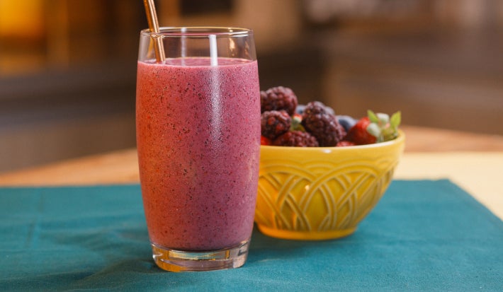 imagem mostra um copo de refresco vermelho cremoso preparado com morangos, amoras e mirtilos