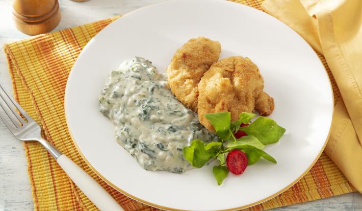 Foto da receita de Creme de Espinafre Sem Lactose. Observa-se um prato branco com o creme do lado esquerdo e, ao lado direito, uma posta de peixe frito com salada.