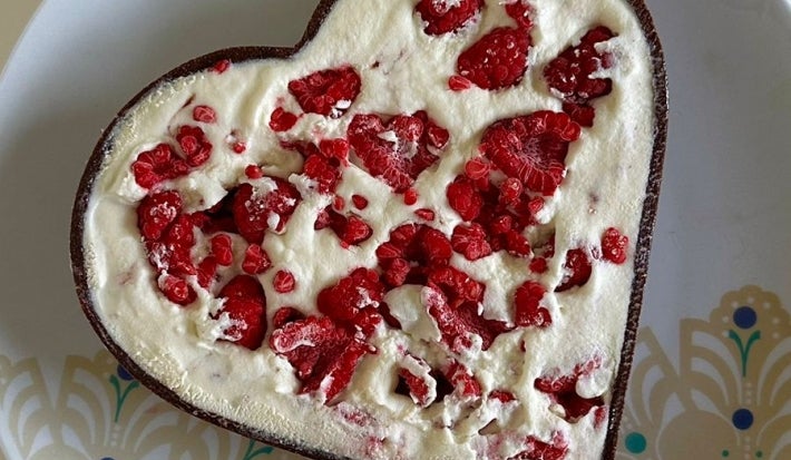 Fotografia vista de cima de uma torta com base crocante de chocolate, recheio de creme branco e várias cortadas junto ao recheio. A torta está sobre um prato grande e raso branco comm detalhes claros.