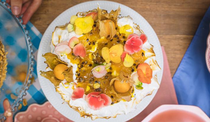 Foto vista de cima do Bolo de Frutas Amarelas, decorado com flores comestíveis, polpa de maracujá e pedaços de manga