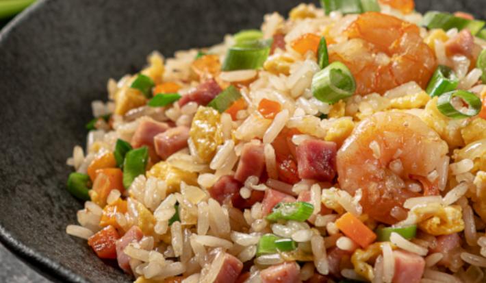 Foto aproximada de um prato preto fundo com a receita de arroz chop suey dentro, decorado com cebolinhas e com camarões e presuntos em cubos.