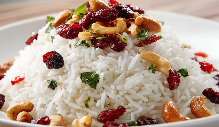 Prato de arroz branco, soltinho, com uma textura leve e fofa, com uvas-passas pretas e castanhas, decorado com cheiro-verde picado.