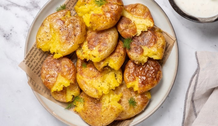 Em cima de uma mesa, prato redondo com batatas ao murro douradas e crocantes.