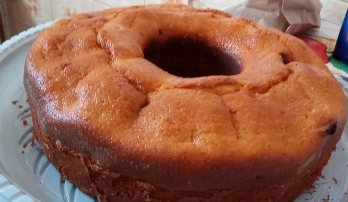 Fotografia de um bolo inteiro de fubá e goiabada sobre um apoio de plástico branco e raso.