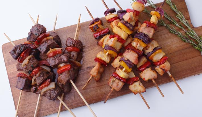 Foto tirada de uma tábua de madeira marrom que contém diversos espetinhos com pedaços de carne