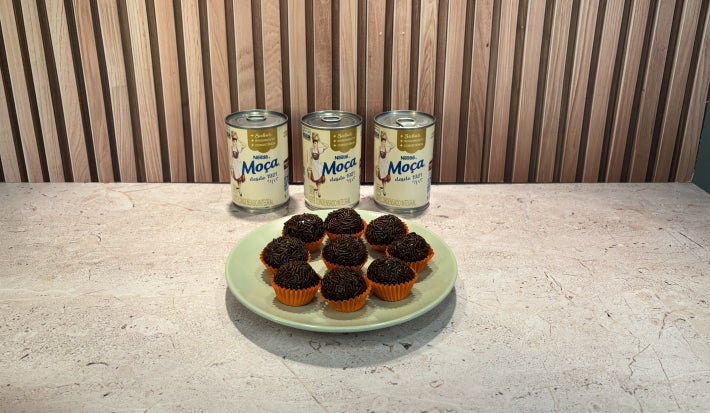 Prato verde-claro com brigadeiros cobertos com granulado de chocolate e latas de Leite Moça ao fundo.