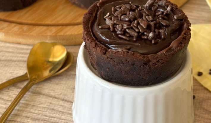Imagem de uma torta pequena redonda com massa de chocolate e recheio sobre um recipiente branco.