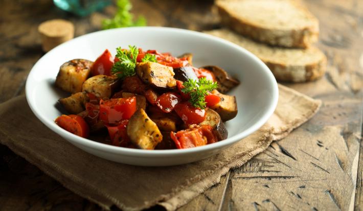 Imagem de um bowl com caponata de berinjela e ao fundo, fatias de pão.