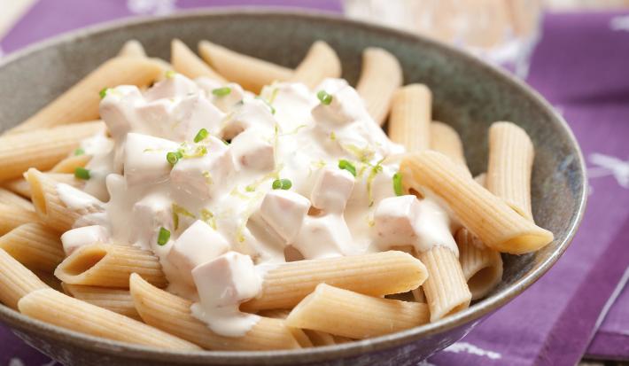 Fotografia em tons de roxo em uma mesa de madeira com um jogo americano roxo e um prato marrom fundo apoiado sobre ele com o penne com molho de limão dentro dele.