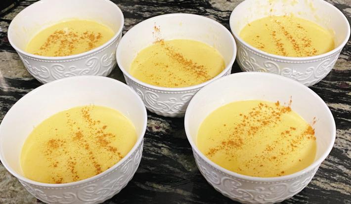Foto de cinco potes brancos com a receita de curau cremoso em tom amarelo, polvilhado com canela em pó