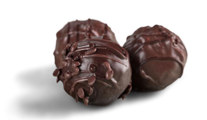 Fotografia de três unidades de bombons de chocolate meio amargo com recheio de purê de goiaba sobre uma mesa branca.