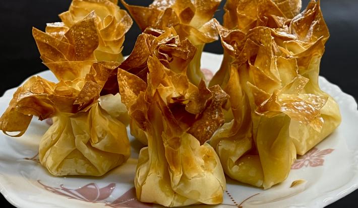 Foto da receita de Trouxinha de Filo com Ovos. Na foto, observa-se 7 trouxinhas assadas em um prato de porcelana branco.