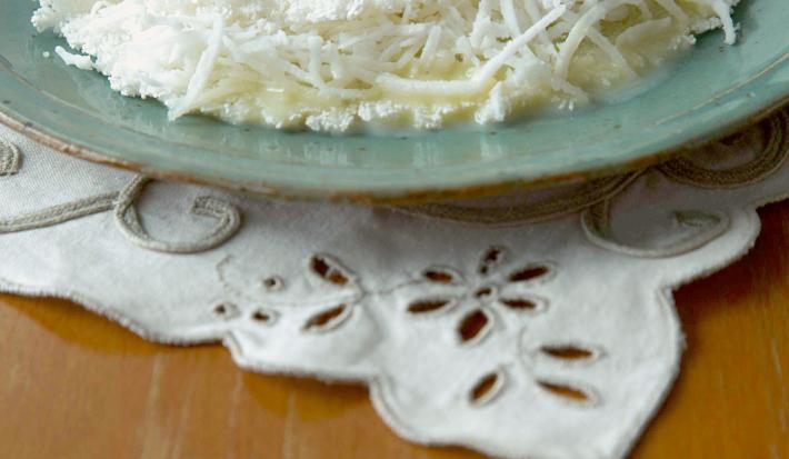 Foto com uma tapioca de Leite Moça e coco em um prato na cor azul, em cima de uma toalha branca decorada