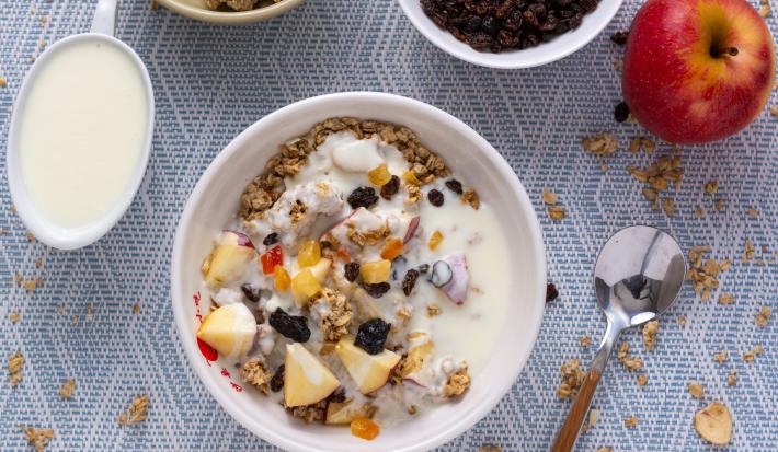 Fotografia em tons de branco com um pote branco ao centro. Dentro do pote existe uma receita de cereal com frutas secas e banana.