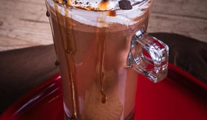 Foto da receita vista de cima de cappuccino crocante servida em uma caneca alta de vidro sobre uma mesa de madeira