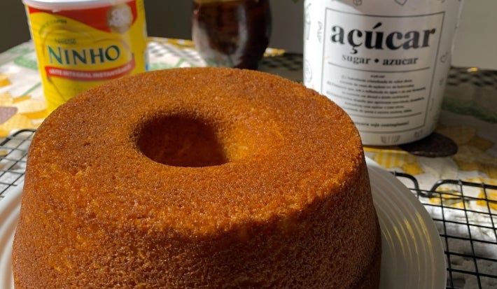 Fotografia de um bolo de ninho inteiro, assado na forma com furo no centro, sobre um prato branco e raso.