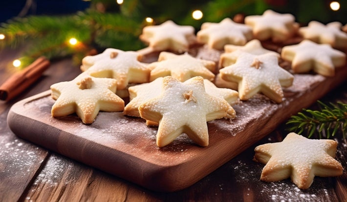 Em cima de uma mesa, prato com biscoitos em formato de estrelas, polvilhados com açúcar de confeiteiro.