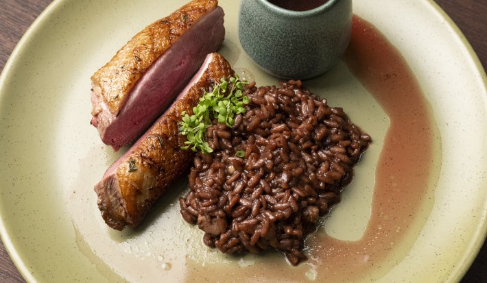 foto da Receita de Pato Selado com Risoto de Vinho Tinto, Alho Negro e Chocolate servido em um prato redondo e vista de cima