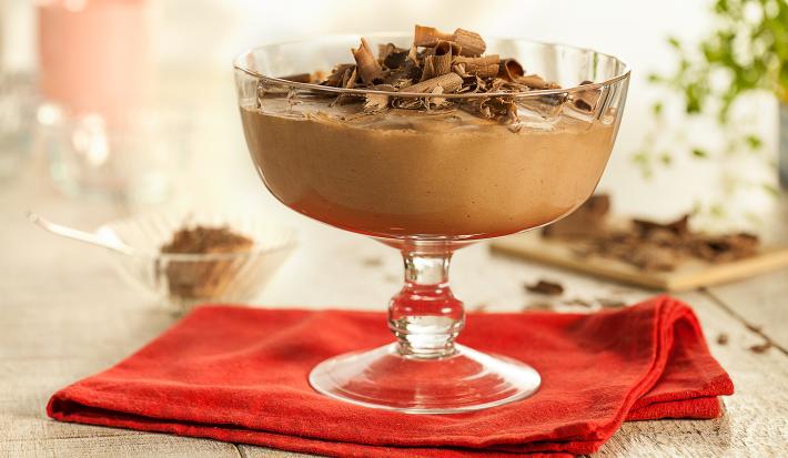 Fotografia em tons de vermelho em uma bancada de madeira com um pano vermelho, uma taça de vidro com a mousse de chocolate dentro dele, decorado com raspas de chocolate. Fotografia em tons de vermelho em uma bancada de madeira com um pano vermelho, uma taça de vidro com a mousse de chocolate dentro dele, decorado com raspas de chocolate.