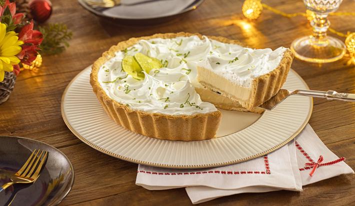 Imagem de uma torta de limão em um prato branco e uma fatia na espátula com decoração de Natal.