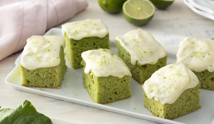 Foto de receita de Bolo de Couve com Calda de Limão. Observa-se uma tábua branca com 6 pedaços de bolo verde com calda de limão.