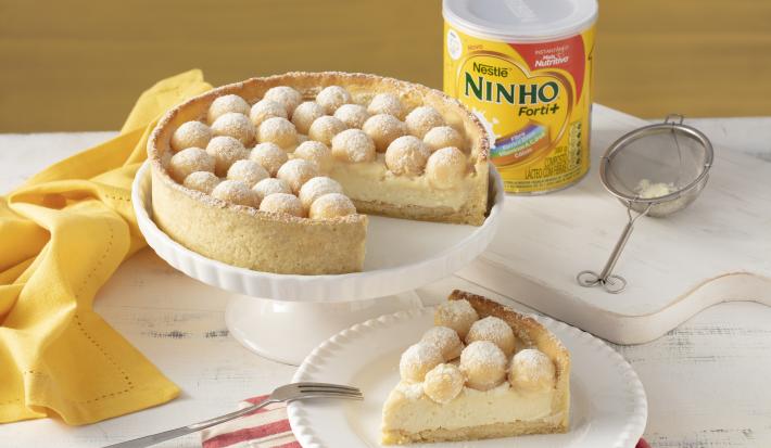 Fotografia em tons de branco e laranja de um prato redondo laranja com uma torta com recheio branco e brigadeiros brancos enrolados.