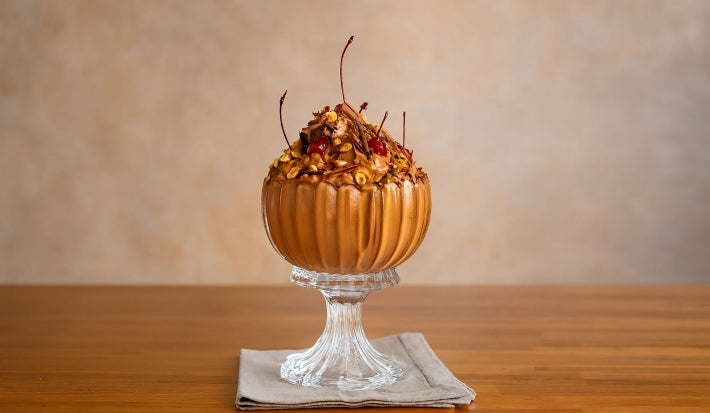 Fotografia em tons claros da Mousse Floresta Negra cremosa e aerada, servida em taça de vidro, decorada com cerejas, avelãs tostadas e raspas de chocolate. Uma sobremesa elegante, perfeita para impressionar em ocasiões especiais!