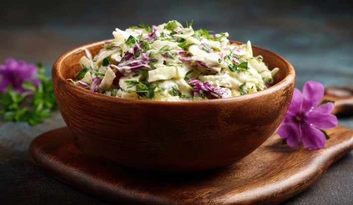 Fotografia de uma salada colorida em uma tigela de madeira, com repolho verde e roxo, ervas frescas e um molho cremoso.