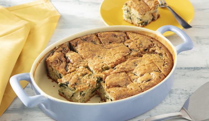 Foto da receita de Torta de Legumes de Liquidificador. Observa-se um refratário oval branco com a torta assada dentro, cortada em fatias quadradas. Atrás, um pratinho amarelo com uma fatia da torta.