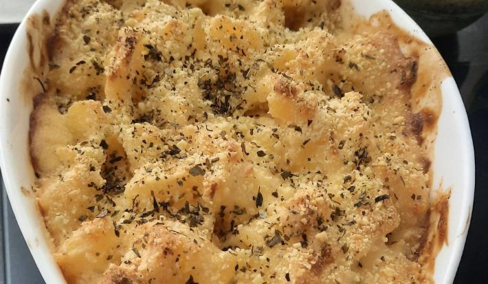 Foto da receita de Aipim Gratinado. Observa-se uma travessa oval com a receita dentro, dourada e polvilhada com orégano.