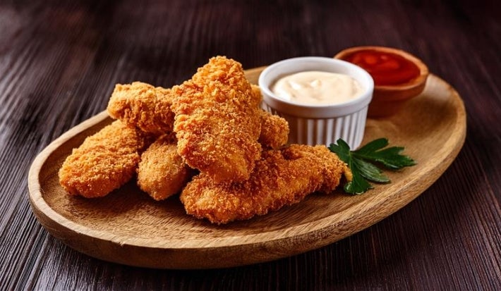 Fotografia mostra tiras de frango empanado e molhos ao lado.