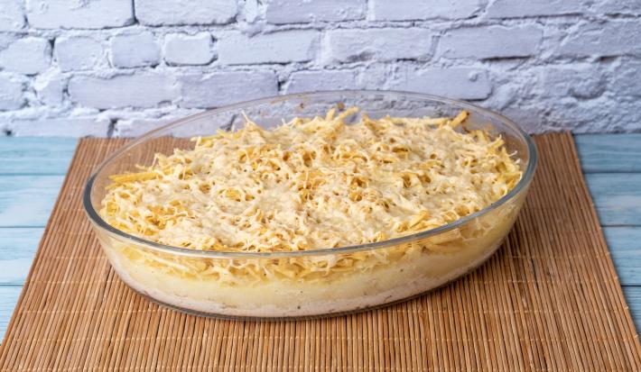 Fotografia em tons de marrom com um recipiente de vidro ao centro. Dentro do recipiente existe uma receita de frango cremoso temperado com legumes e salsinha.