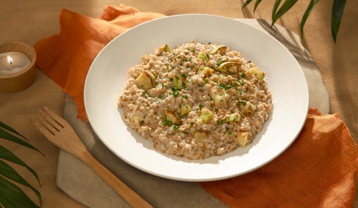 Foto da receita de risoto de abobrinha vegano servida em um prato de cerâmica com um garfo de madeira ao lado sobre um paninho laranja