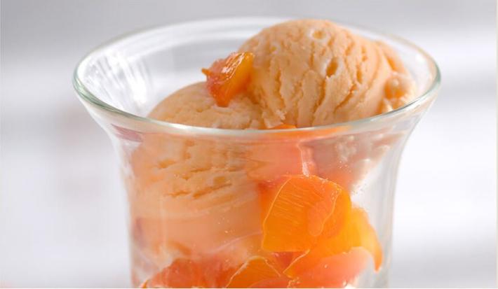 foto tirada de um copo transparente com bolas de sorvete de caqui e pedaços da fruta.